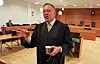 Advokat Nicolay Skarning står i en rettssal med dokumenter og en kopp.