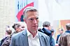 Gråhåret mann i dress foran Stortinget, omgitt av mennesker og norske flagg.