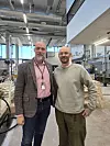 To menn står side ved side i et moderne verksted med arbeidsbenker og teknisk utstyr.