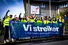 Streikende arbeidere i verneklær holder et «Vi streiker»-banner foran et Equinor-anlegg.