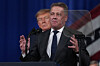 Gernot Döllner taler ved en talerstol mens Donald Trump står bak ham foran amerikanske flagg.
