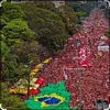 Stor folkemengde med røde flagg og brasiliansk flagg i en treomkranset gate.